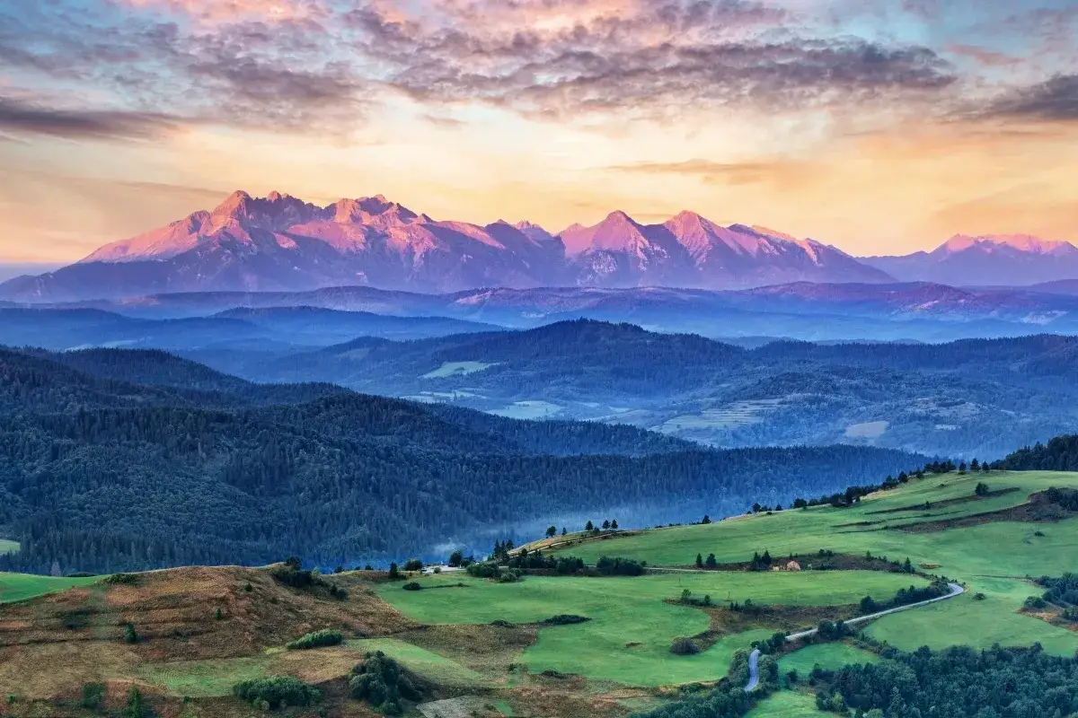 Tatry o zachodzie słońca, jedno z **10 najpiękniejszych miejsc w Polsce**. Góry w odcieniach różu i fioletu, zielone wzgórza i lasy.