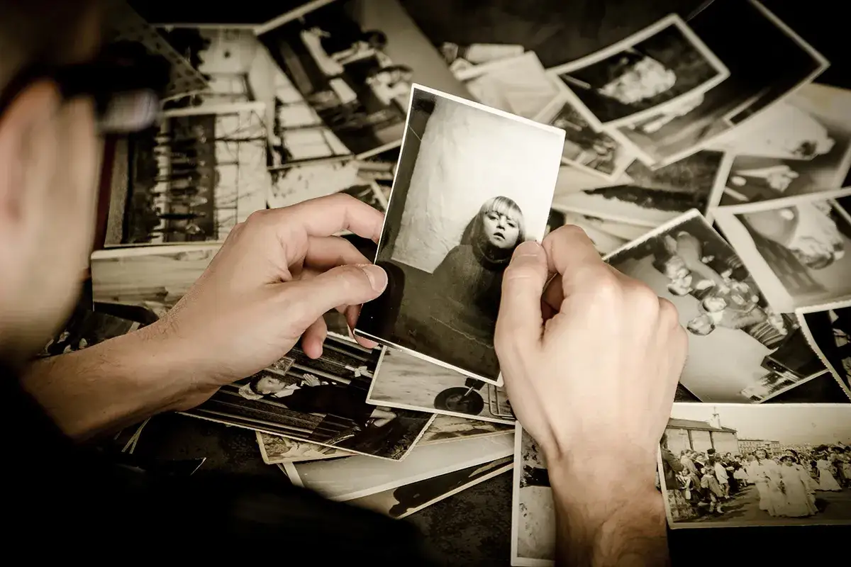 Ręce przeglądają stare fotografie, tworząc osobistą archiwizację zdjęć. Widać portret dziecka i grupowe ujęcia.