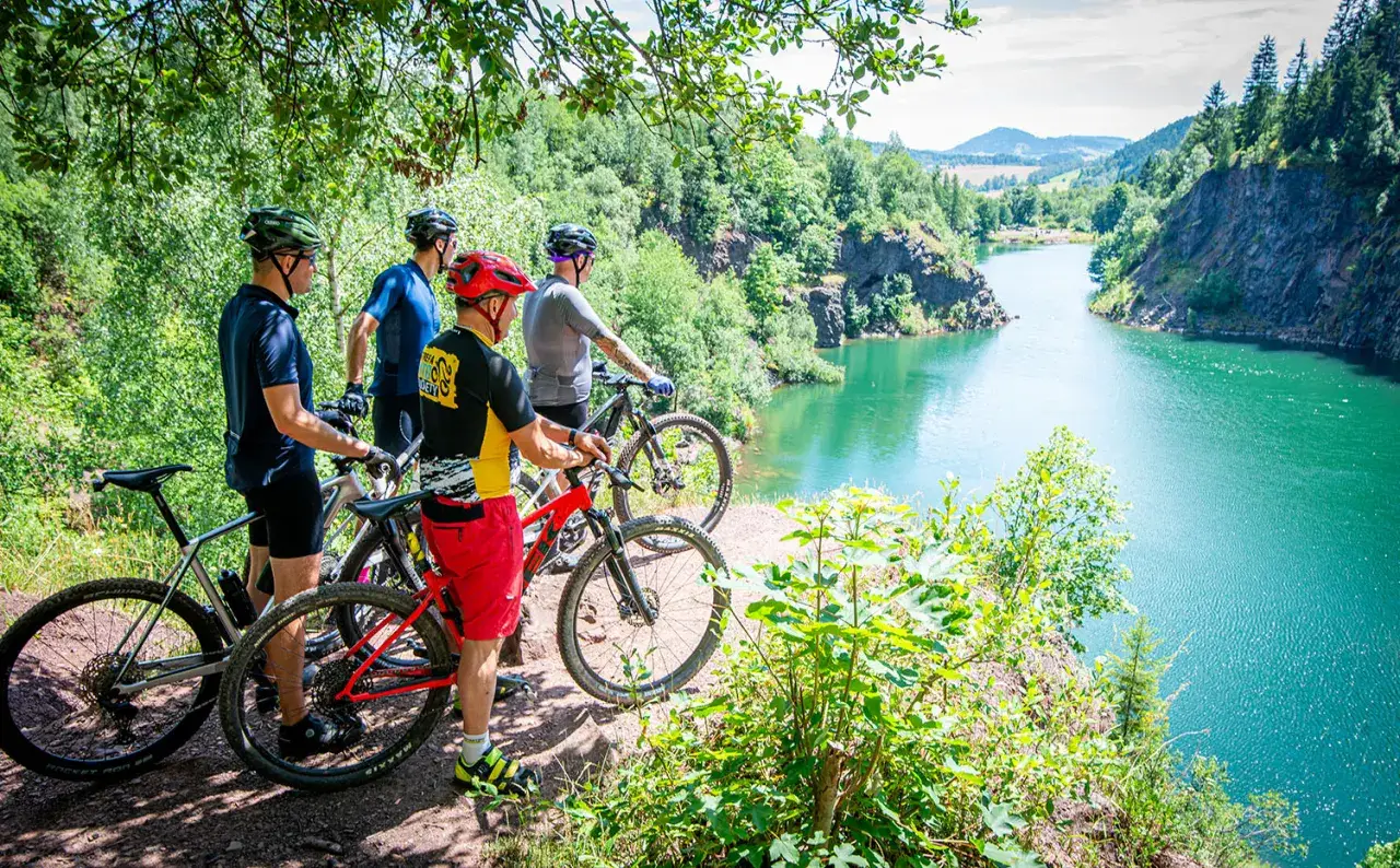 Czterech rowerzystów MTB podziwia malowniczy widok na turkusowe jezioro w Sudetach. Idealne miejsce na rowerową przygodę.