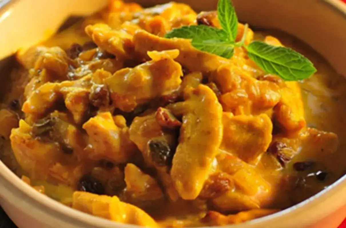 Pyszny kurczak w sosie curry z rodzynkami, ozdobiony listkiem mięty. Idealny przykład, jak zrobić sos curry do kurczaka.
