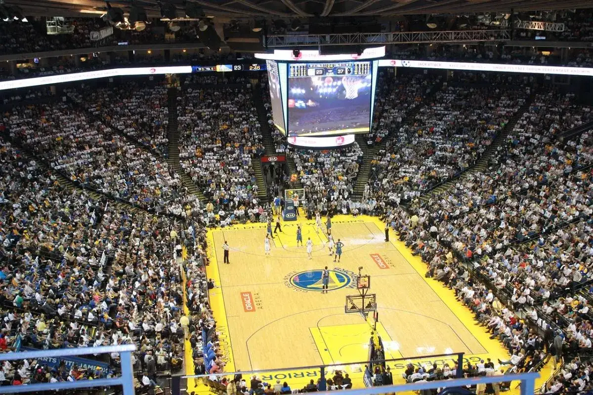Mecz koszykówki w Oracle Arena. Na boisku gracze, na trybunach tłumy kibiców. Na telebimie widać wynik, który sugeruje, że gra jest w końcowej fazie, być może ostatni z czterech kwart.