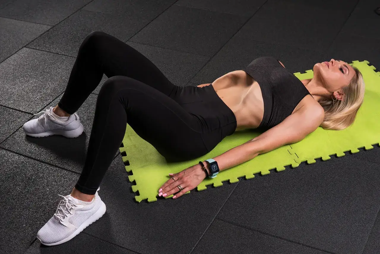 Kobieta na macie wykonuje ćwiczenia vacuum, napinając mięśnie brzucha.