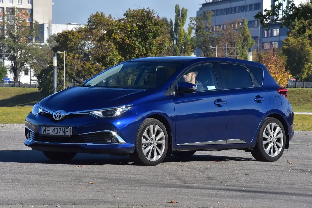 Niebieska Toyota Auris Hybrid, z kierowcą za kierownicą, na parkingu. Zastanawiasz się, ile pali Toyota Auris Hybrid?