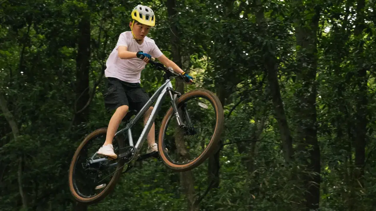 Chłopiec w kasku wykonuje skok na rowerze na leśnej ścieżce. To prawdziwy rower na hopy!