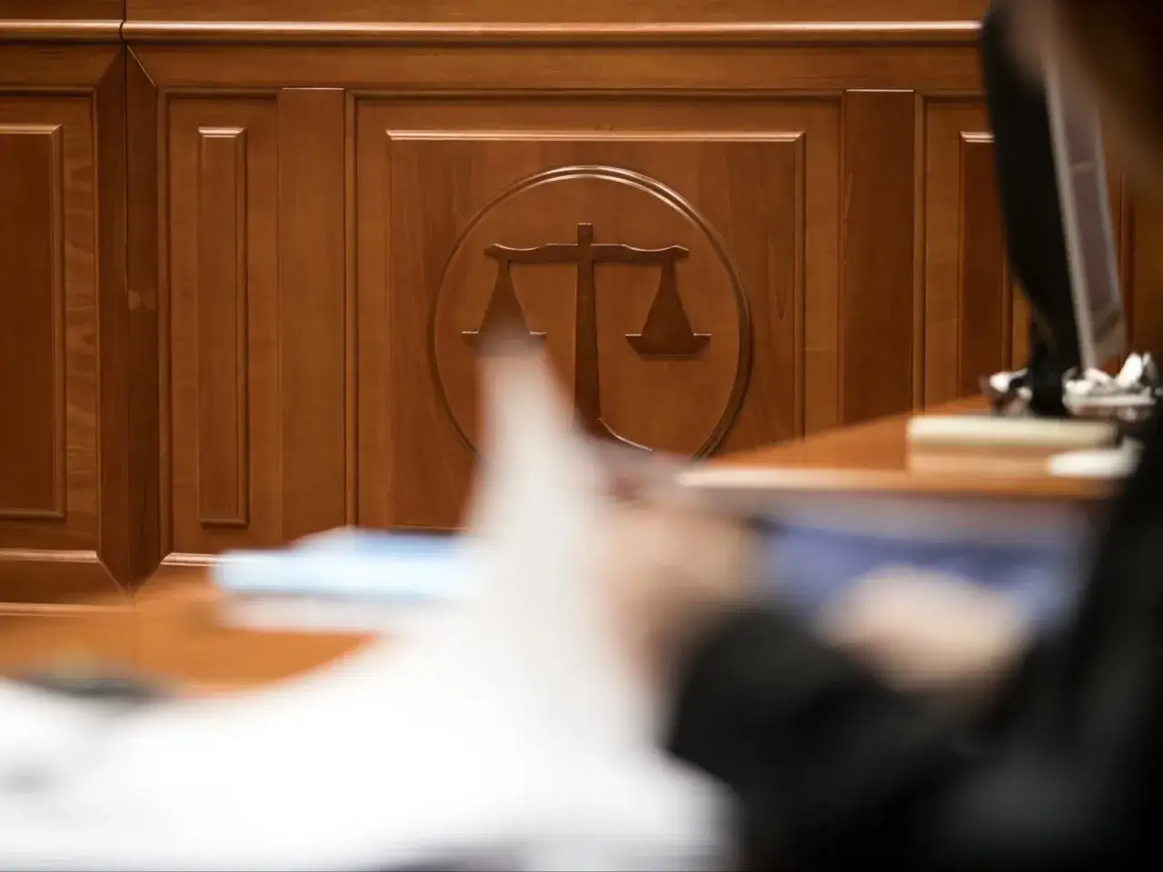Drewniana ściana z symbolem wagi sprawiedliwości. Zastanawiasz się, ile czeka się na rozprawę w sądzie cywilnym? Czas oczekiwania bywa długi.