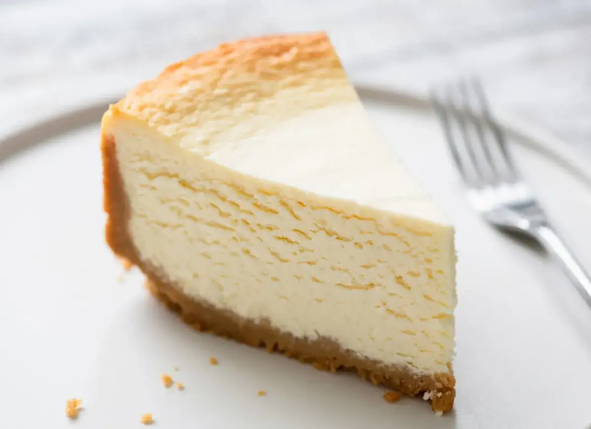 Kawałek kremowego sernika na kruchym spodzie, idealny jako alternatywa dla budyniu. Obok widelczyk.