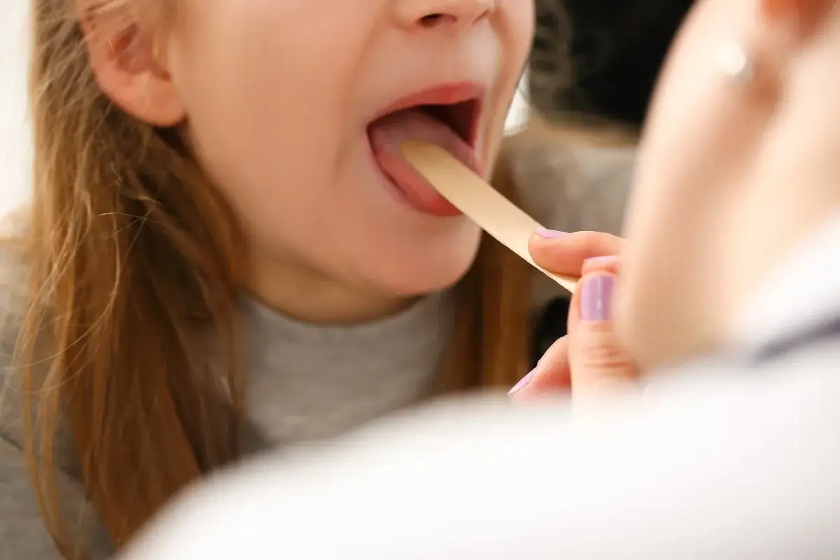 Lekarz bada gardło dziecka, szukając odpowiedzi na pytanie, co na ból gardła u dziecka.
