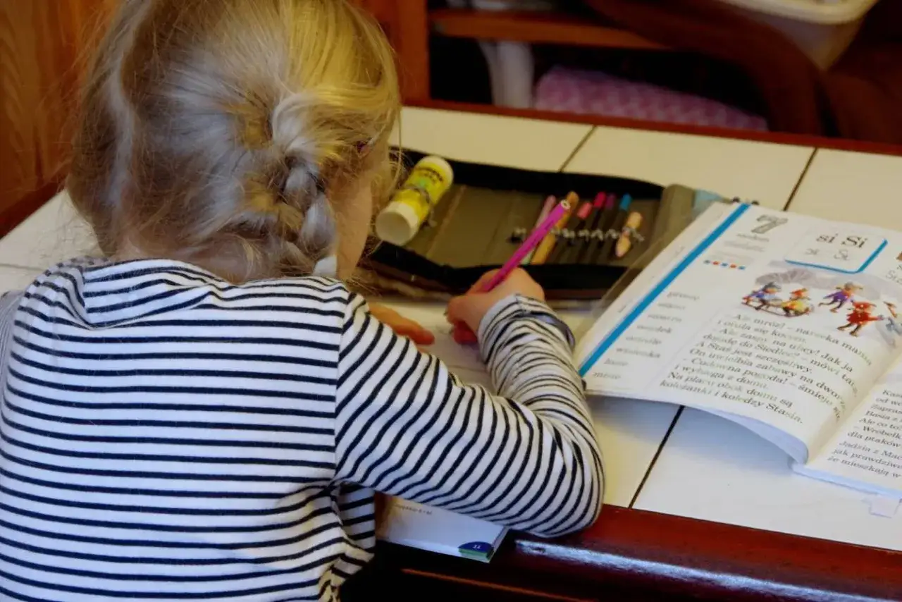 Dziewczynka z warkoczem pisze w książce. Ile godzin nauczania indywidualnego potrzebuje, by tak pięknie czytać?