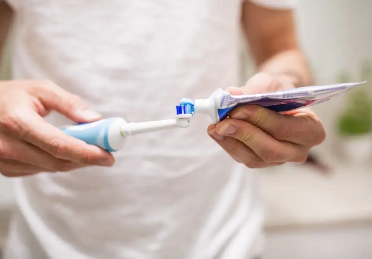 Przygotowanie do mycia zębów szczoteczką soniczną: nakładanie pasty na główkę.