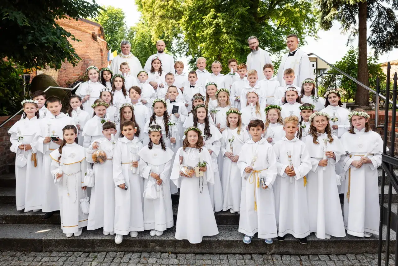 Dzieci w białych strojach komunijnych, z wiankami na głowach, pozują do zdjęcia. Zastanawiasz się, ile kosztuje fotograf na komunię?