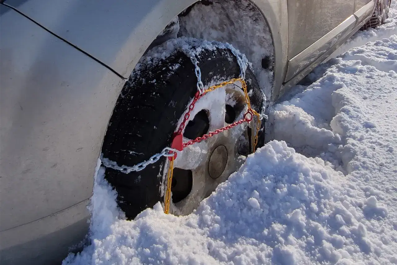 Samochód w zaspie, na kole założone łańcuchy. Uniknij mandatu za brak łańcuchów w Polsce, przygotuj się na zimę!