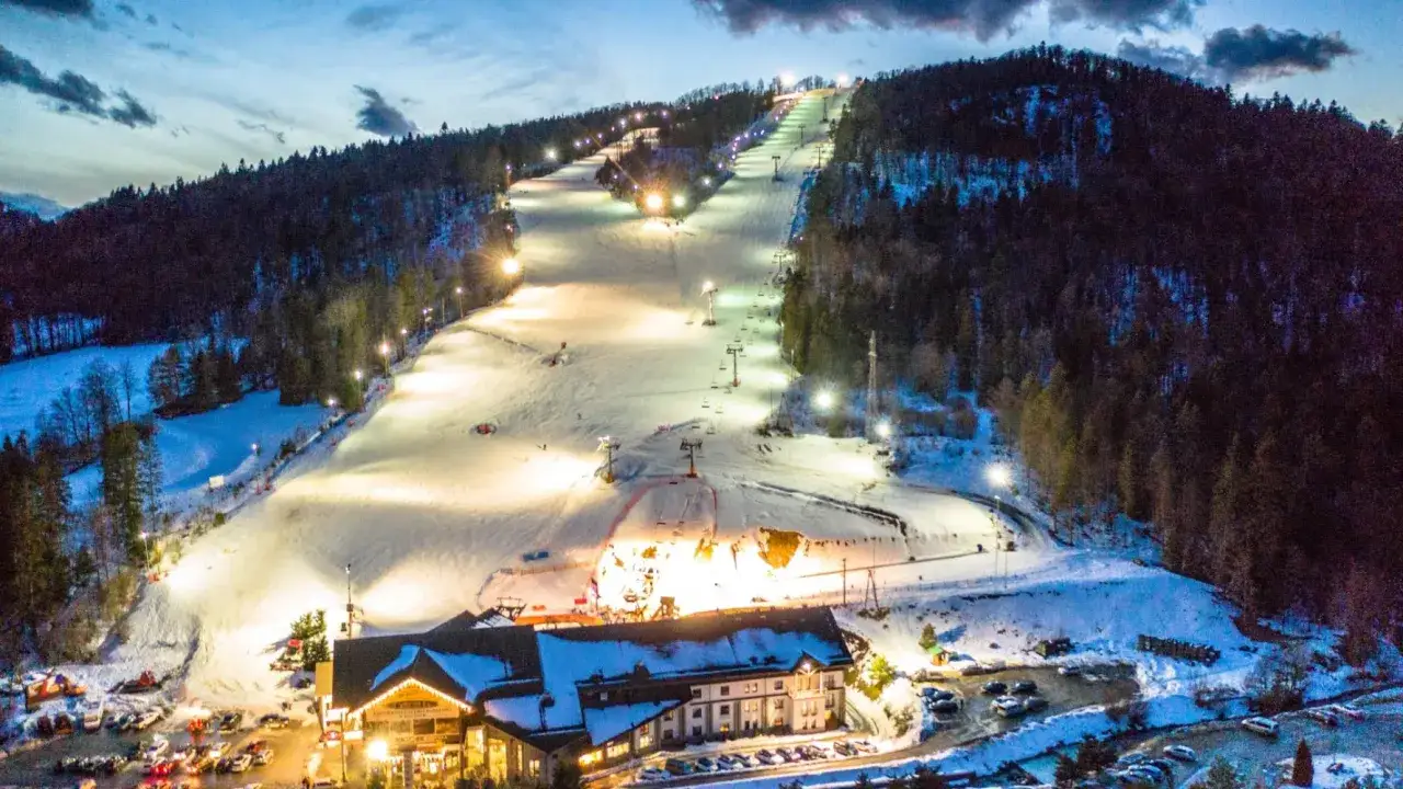Oświetlony stok narciarski z wyciągami i hotelem u podnóża. Idealne miejsce, gdzie na ferie zimowe.