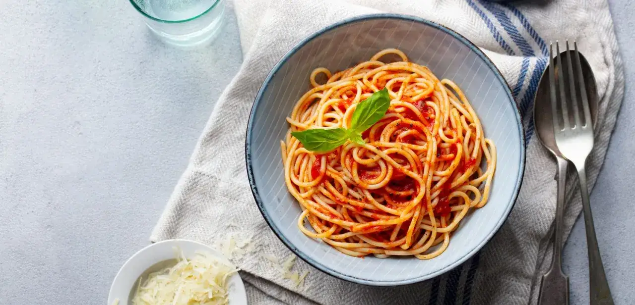 Misternie ułożone spaghetti z sosem pomidorowym i listkiem bazylii. Obok miseczka z tartym parmezanem. Idealne pytanie: jakie przyprawy do spaghetti?