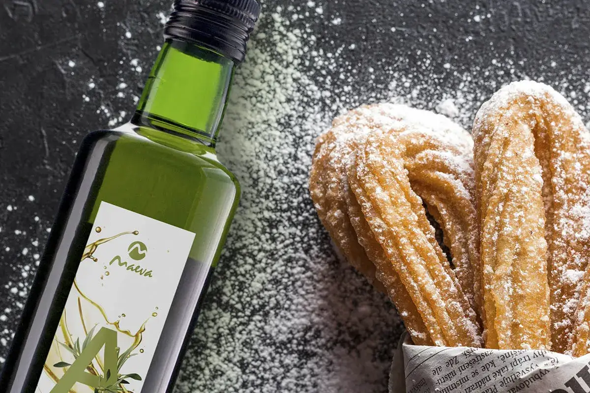 Botella de aceite de oliva junto a churros espolvoreados con azúcar glas.