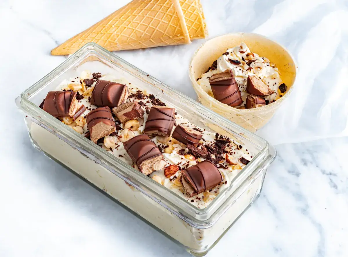 Lody Kinder Bueno w pojemniku i wafelku, posypane orzechami i czekoladą.