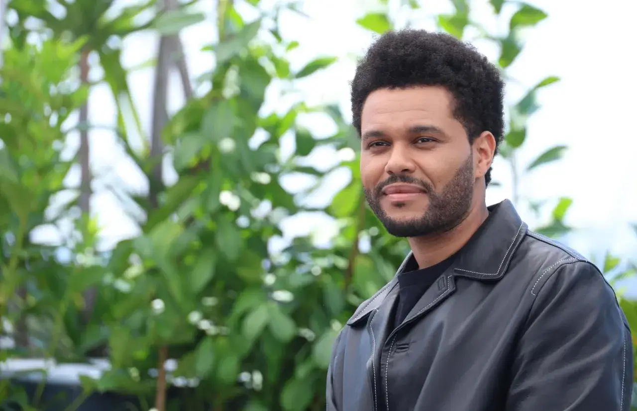 The Weeknd trägt eine schwarze Lederjacke vor einem grünen, unscharfen Hintergrund.