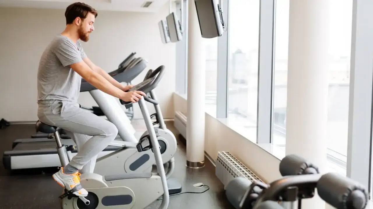 Mężczyzna ćwiczy na rowerze stacjonarnym w siłowni.
