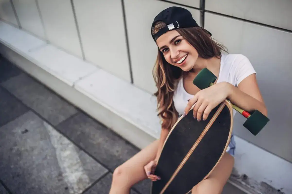Uśmiechnięta dziewczyna w czapce z daszkiem trzyma longboard.
