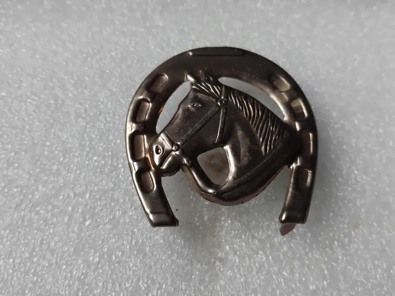 Metalowa odznaka w kształcie podkowy z głową konia.