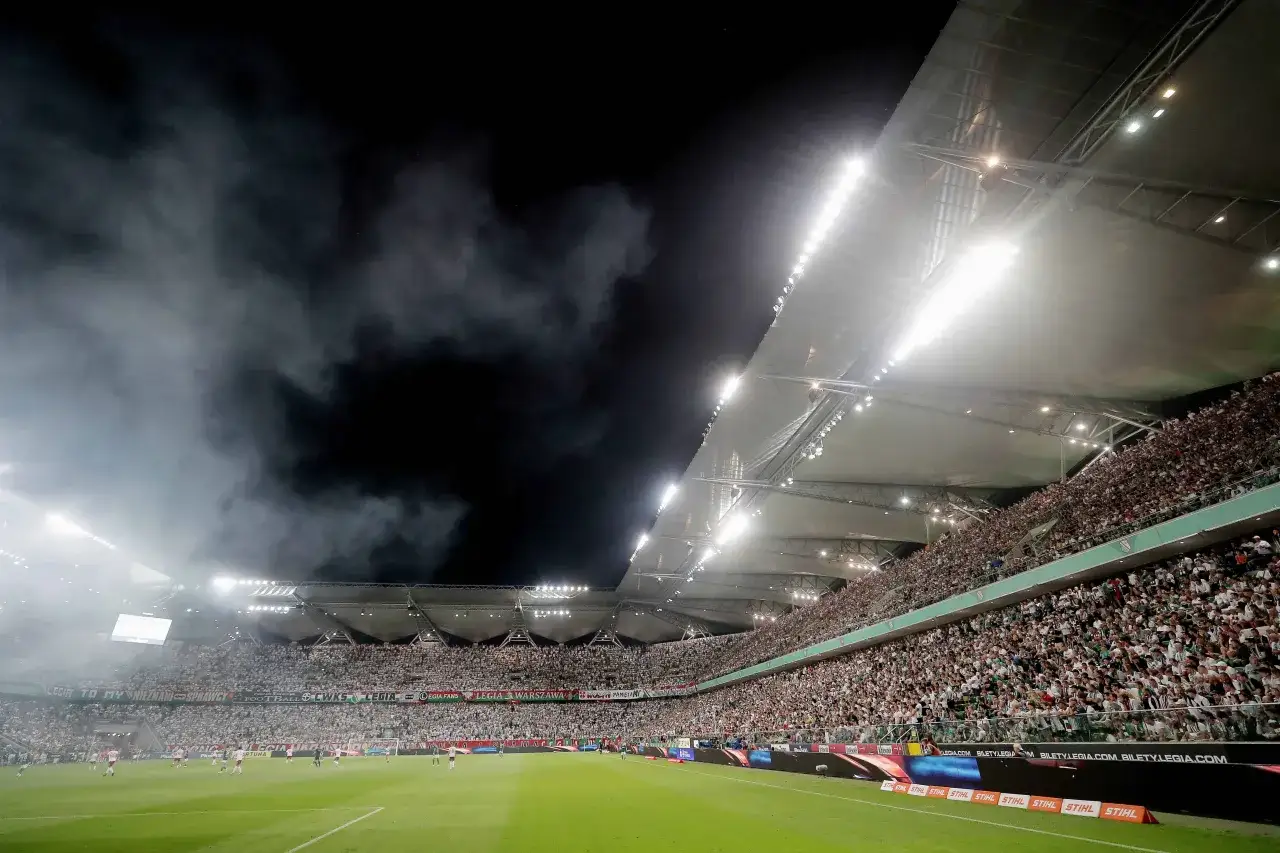 Stadion Legii nocą, pełne trybuny, dym i światła.
