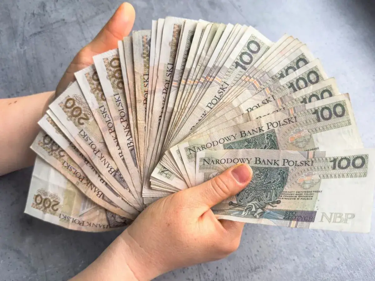 Dłonie trzymające wachlarz polskich banknotów 100 i 200 zł.