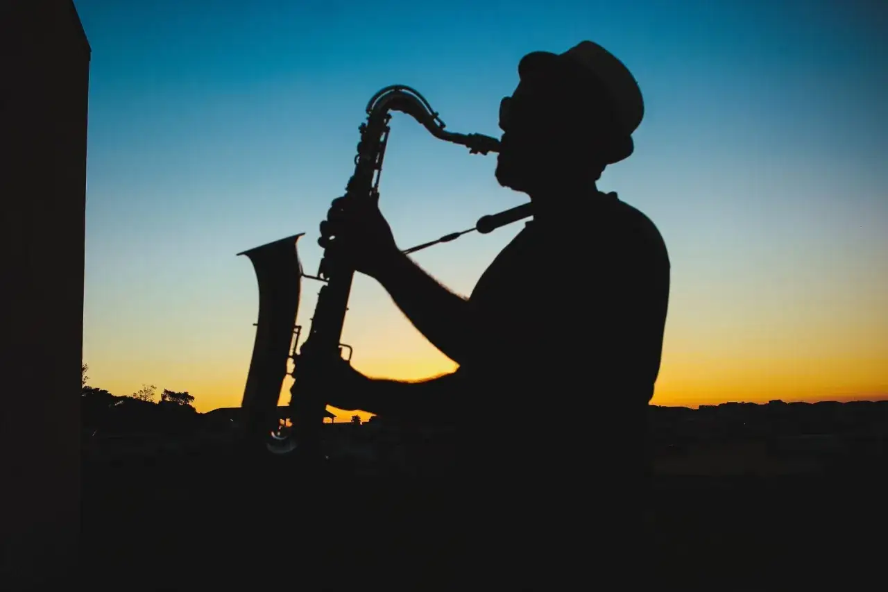 Sylwetka muzyka w kapeluszu grającego na saksofonie o zachodzie słońca. Prawdziwy mistrz, jeden z najlepszych bluesmanów świata.