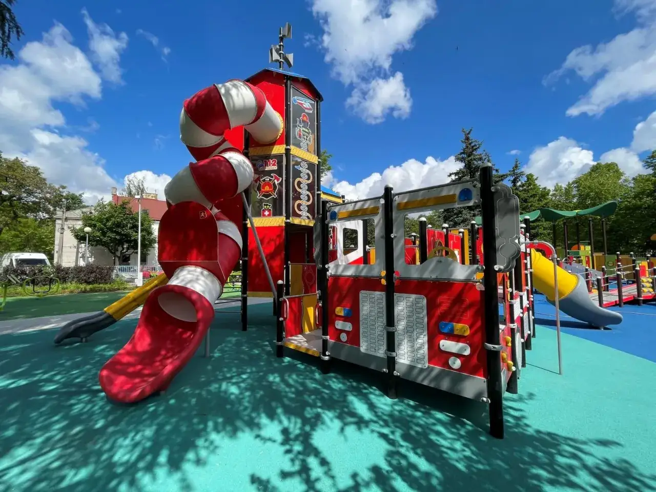 Kolorowy plac zabaw w kształcie remizy strażackiej z rurami i zjeżdżalniami.