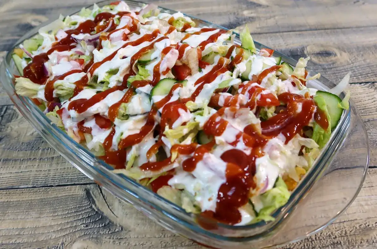 Kapsalon z kurczakiem, sałatą, pomidorami, ogórkiem i sosami w szklanej misce.
