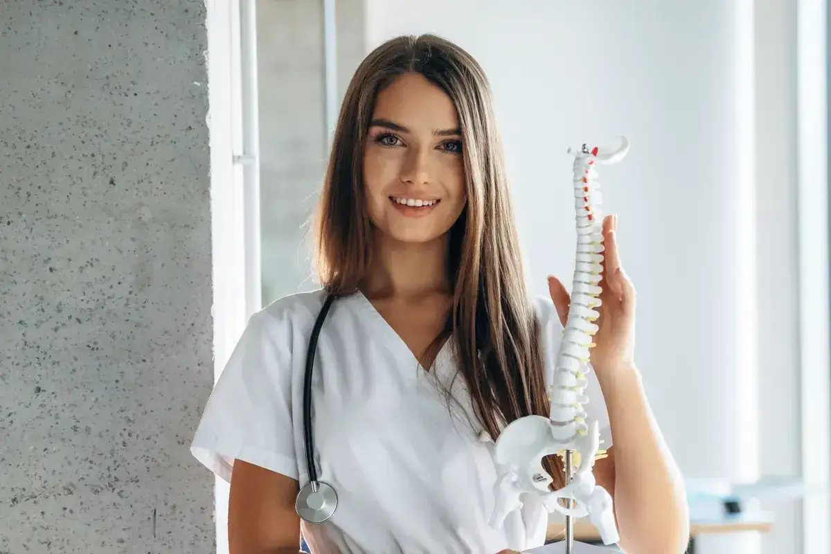 Uśmiechnięta fizjoterapeutka z modelem kręgosłupa. Zastanawia się, do kiedy studia magisterskie fizjoterapia.