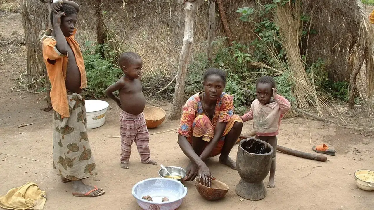 Dzieci i matka w tradycyjnej chacie w Burkina Faso. Kobieta przygotowuje posiłek, a dzieci obserwują.