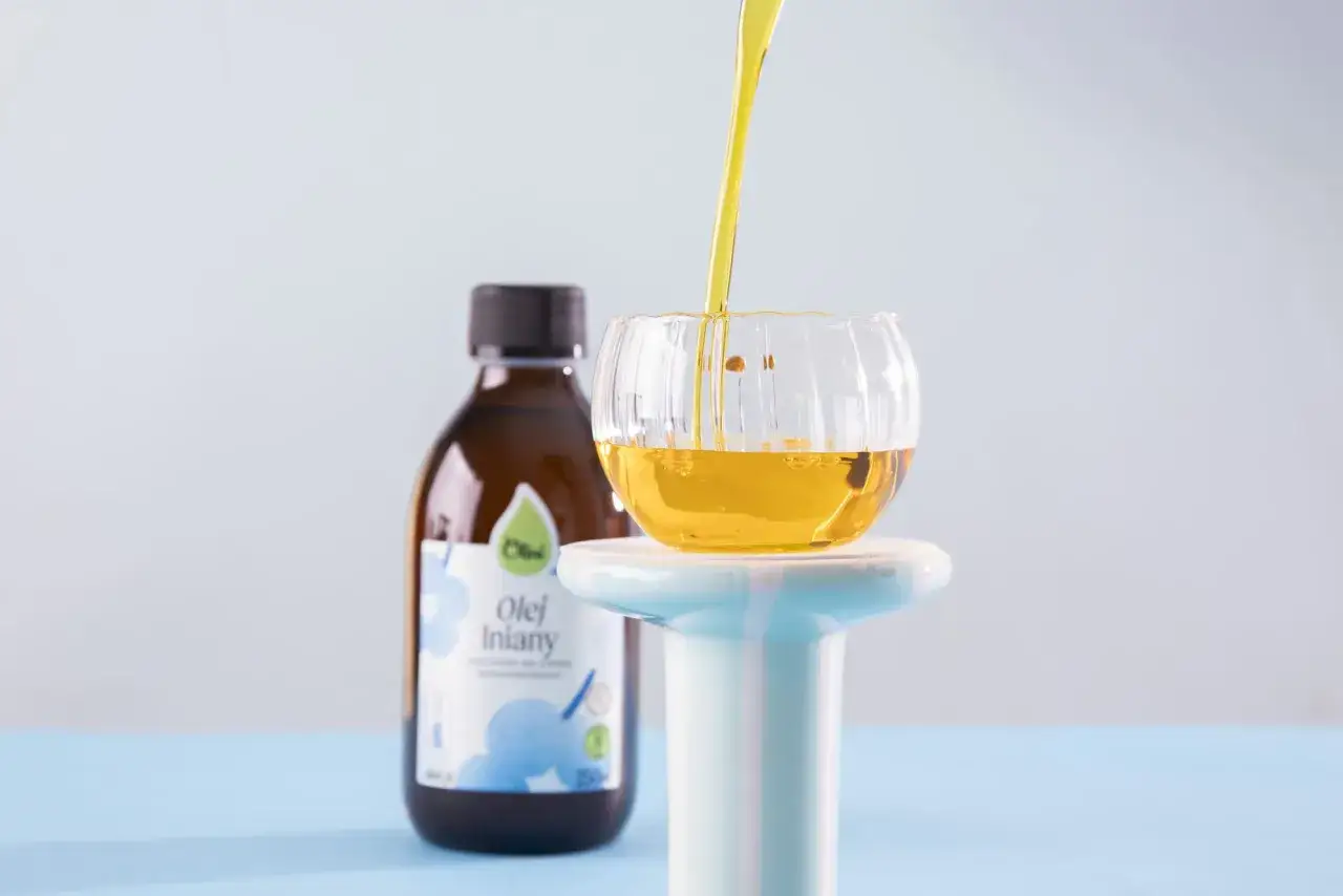 Złocisty olej lniany, znany ze swoich prozdrowotnych właściwości, jest przelewany do szklanej miseczki. Obok stoi butelka z etykietą "Olej lniany".