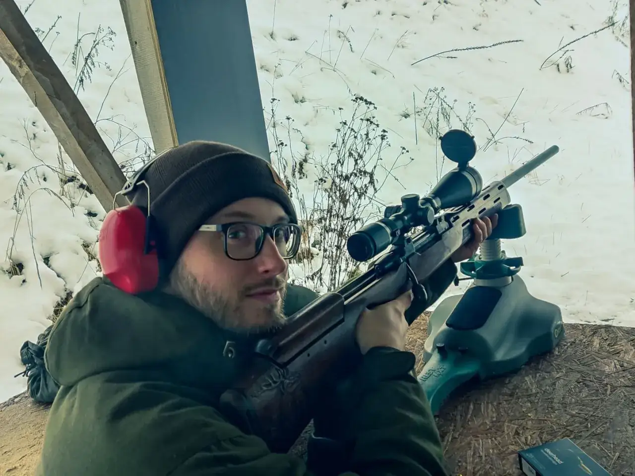 Mężczyzna w okularach i słuchawkach ochronnych celuje z karabinu. Czy myśliwi muszą brać udział w zawodach sportowych? Zima na strzelnicy.