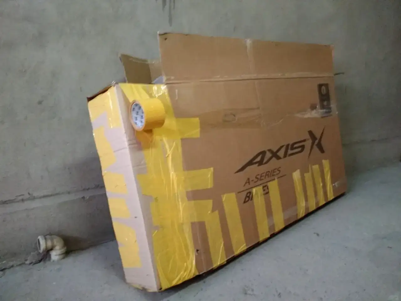 Duże, kartonowe pudło z rowerem, zabezpieczone żółtą taśmą, gotowe do przewozu roweru samolotem.