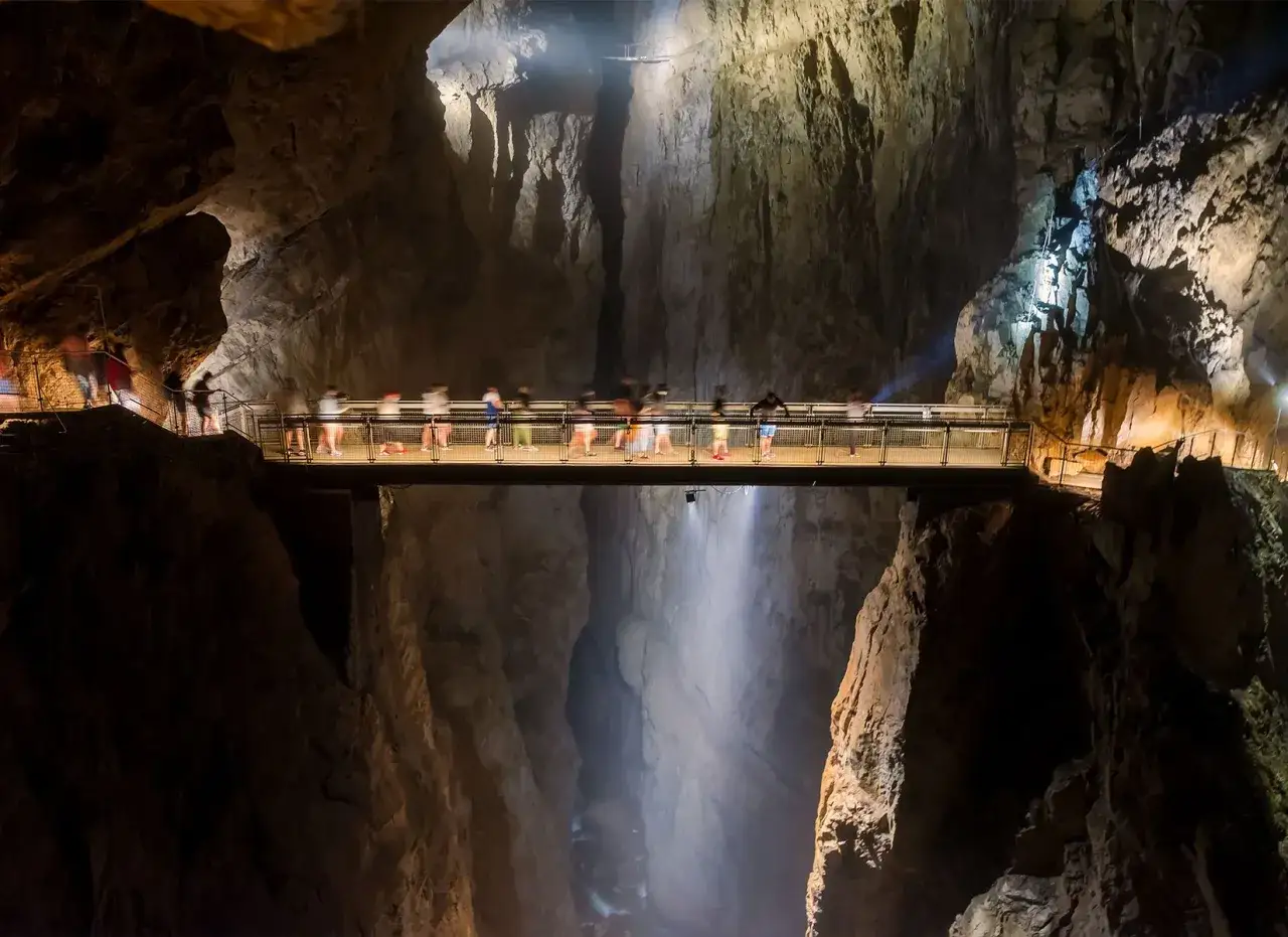 Most turystów przemierza most w słowenii jaskinie szkocjańskie, podziwiając ogromną przepaść i wodospad.
