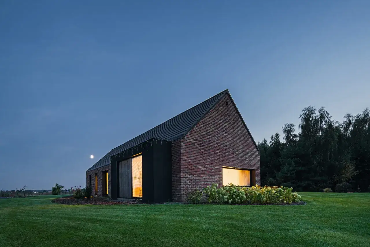 Nowoczesne domy z cegły w otoczeniu zieleni, oświetlone ciepłym światłem.