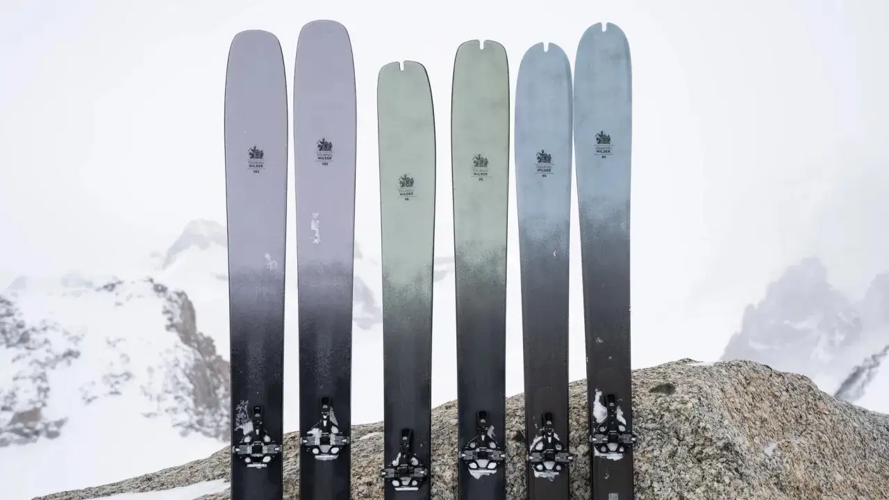 Sześć nart skiturowych o różnej długości, ustawionych na tle zaśnieżonych gór.