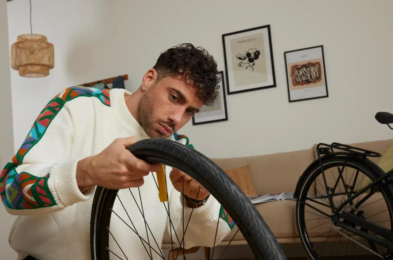 Mężczyzna w kolorowym swetrze uczy się, jak załatać dętkę domowym sposobem, używając żółtego narzędzia do opon.