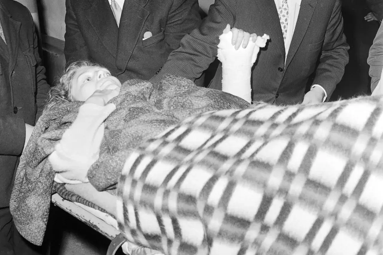Anna German, przykryta kocem, leży na noszach. Jej ręka jest w gipsie, co może sugerować chorobę lub wypadek.