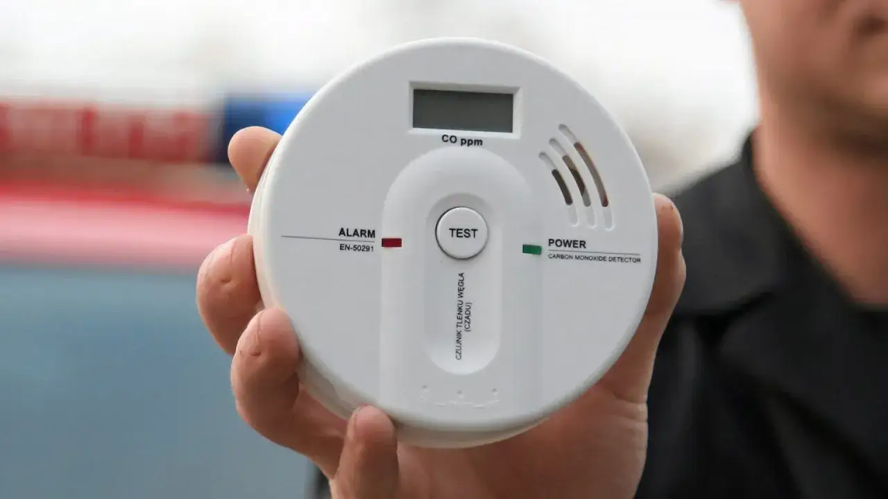 Biały czujnik czadu trzymany w dłoni, z wyświetlaczem CO ppm i przyciskiem TEST.