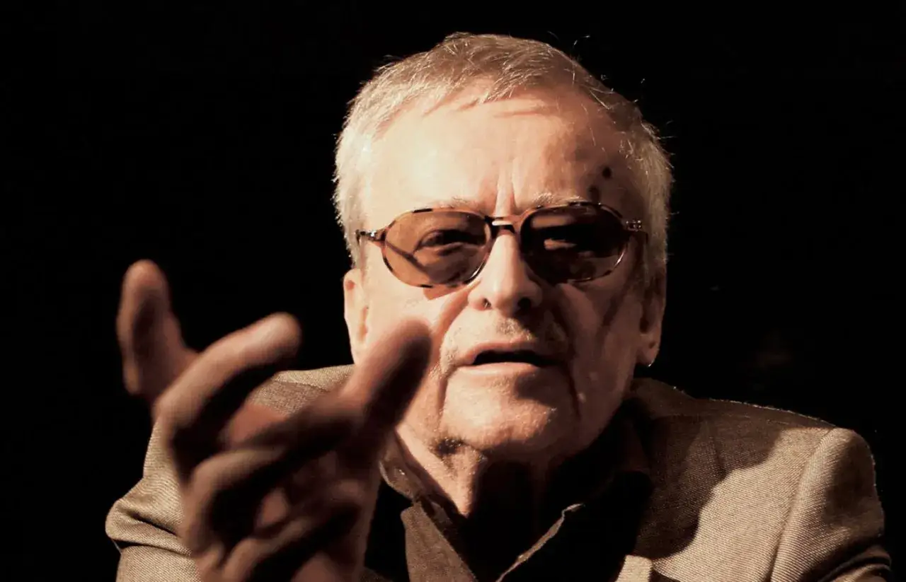 Jerzy Jarocki w okularach, z gestem dłoni, w ciemnym tle.