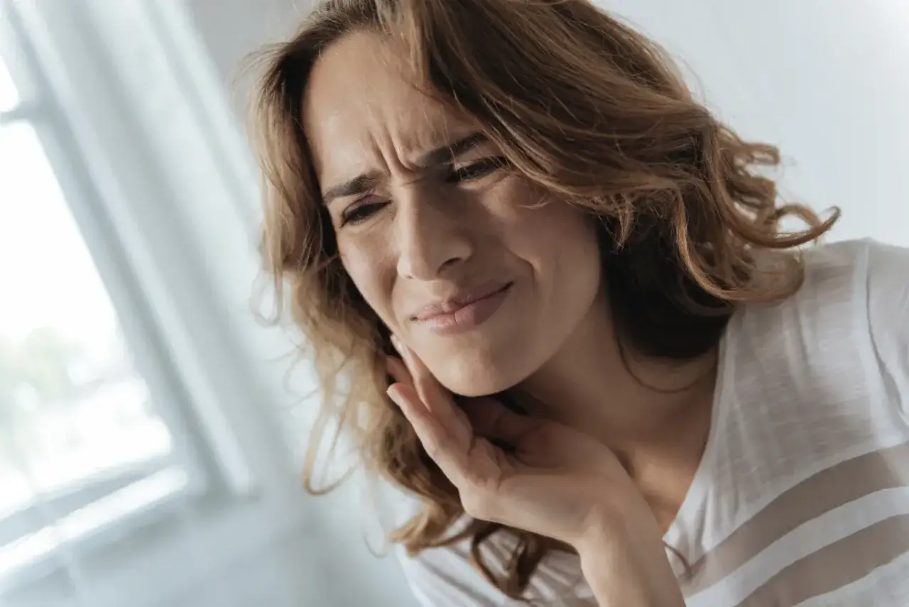 Kobieta z wykrzywioną twarzą, trzymająca się za policzek, cierpi z powodu wędrującego bólu zębów.