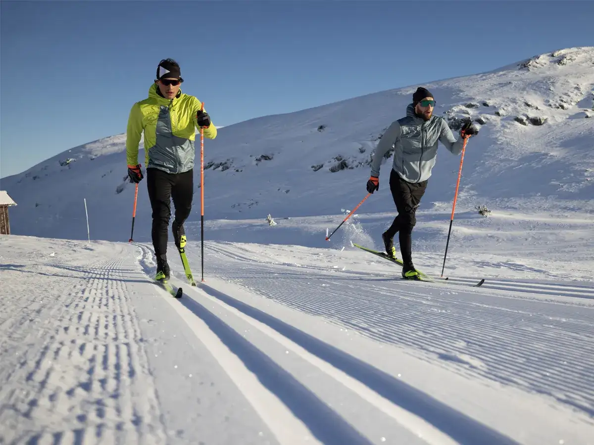 Dwóch mężczyzn na nartach biegowych dla początkujących, pokonujących ośnieżony stok.