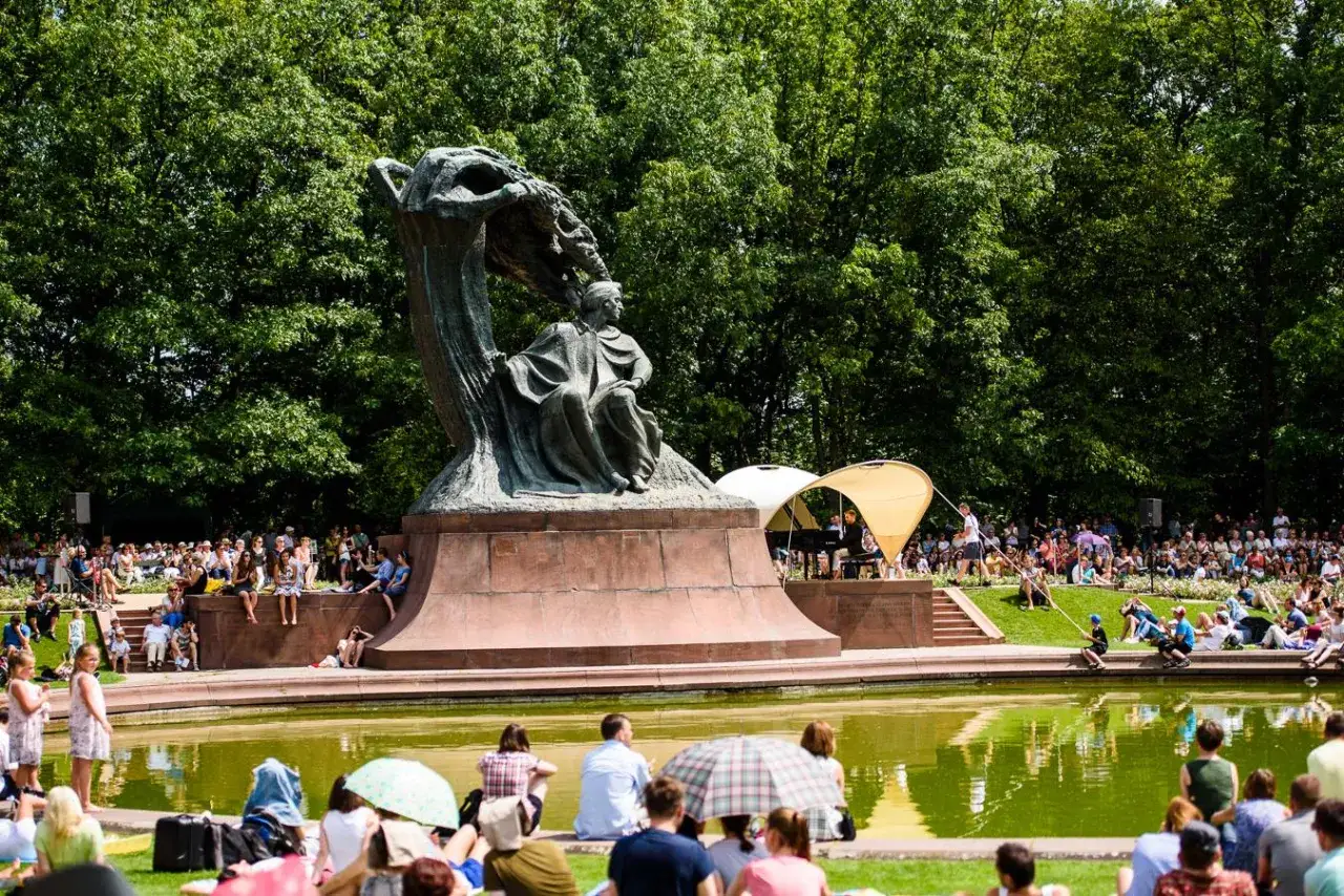 Koncert chopinowski w Łazienkach Królewskich. Tłumy słuchają muzyki przy pomniku Chopina.