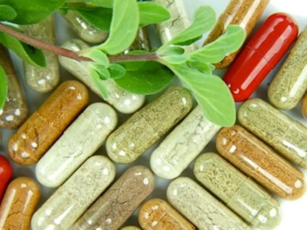 Cápsulas de suplementos naturales de varios colores y hojas verdes.