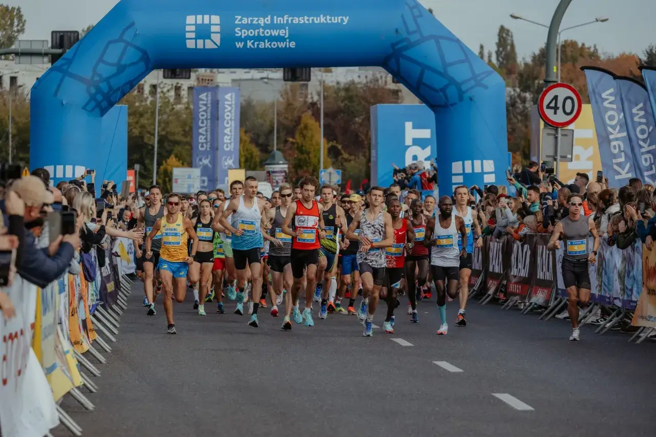 Biegacze przekraczają niebieską bramę startową maratonu w Krakowie. Zastanawiasz się, ile trwa maraton? Ci zawodnicy dopiero zaczynają swoją drogę.