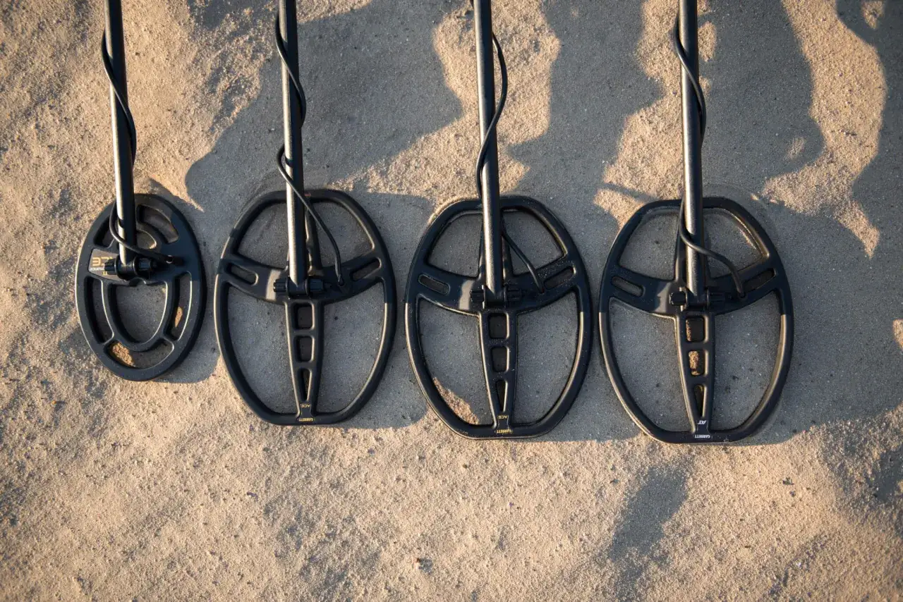 Cztery cewki wykrywaczy metali leżące na piasku.