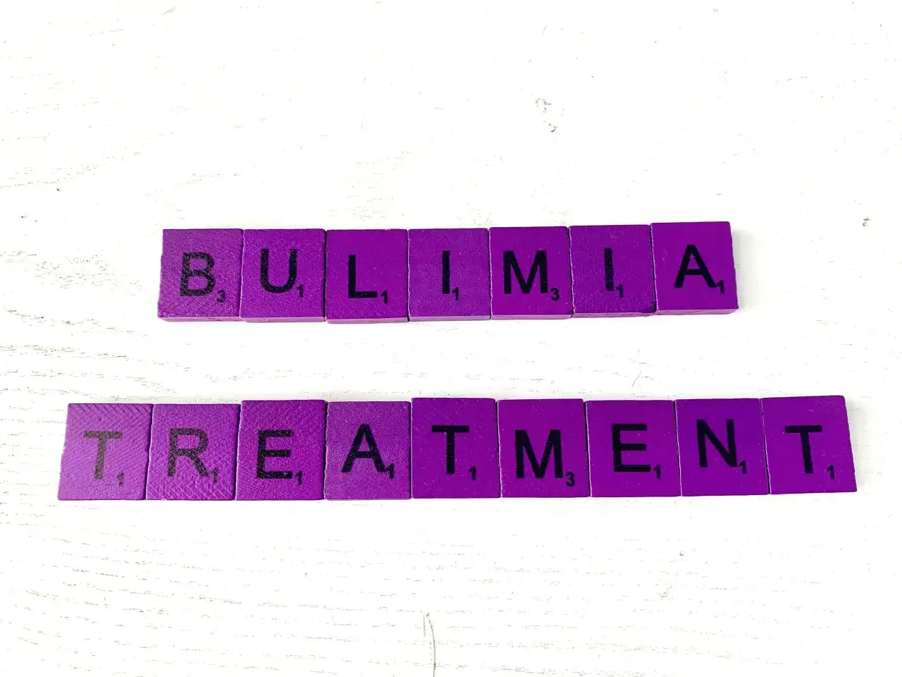 Fioletowe kafelki z literami układają słowa "BULIMIA TREATMENT". Bulimia co to? Leczenie jest kluczowe.