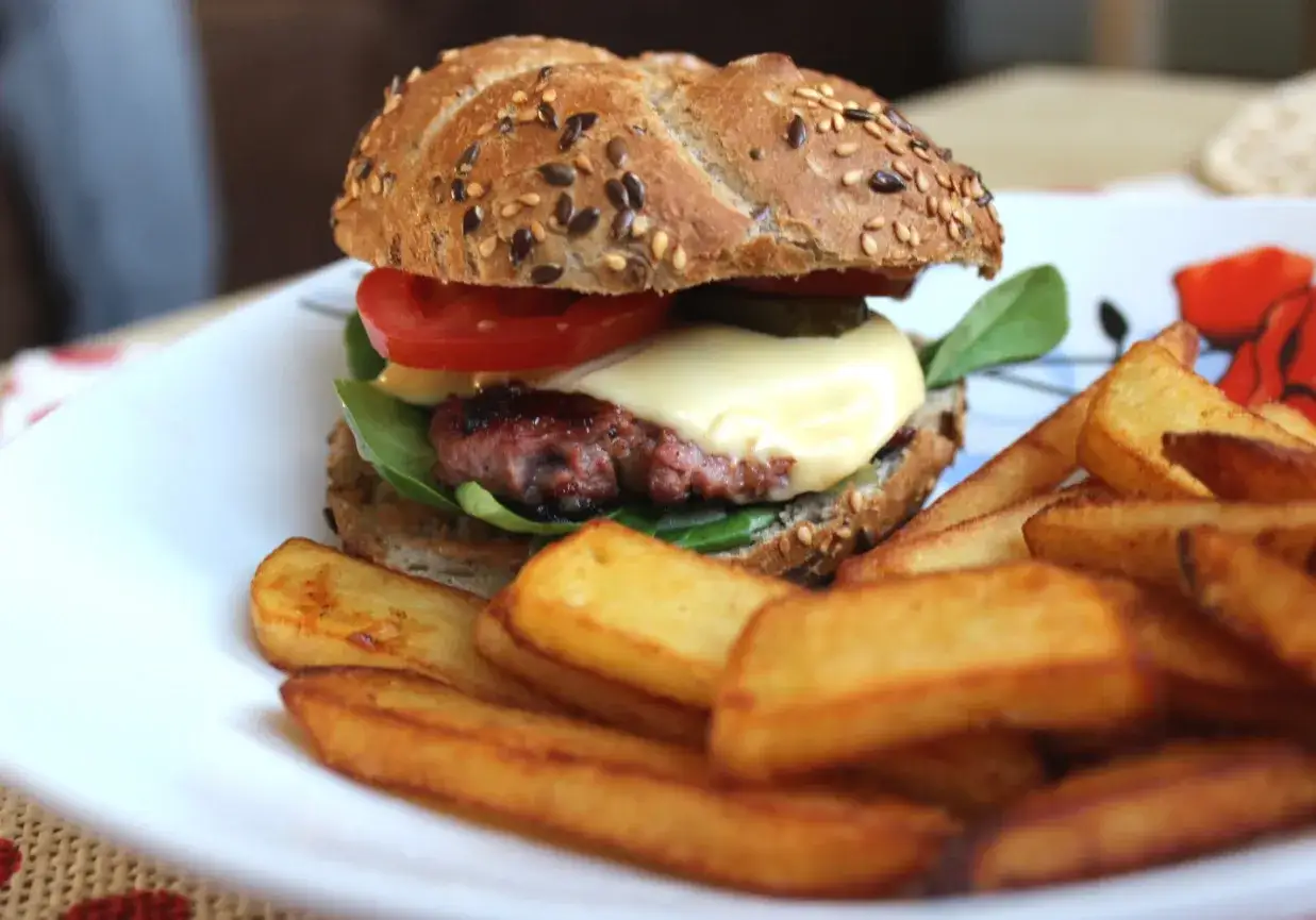 Soczysty domowy burger wołowy z serem, pomidorem i frytkami na talerzu.