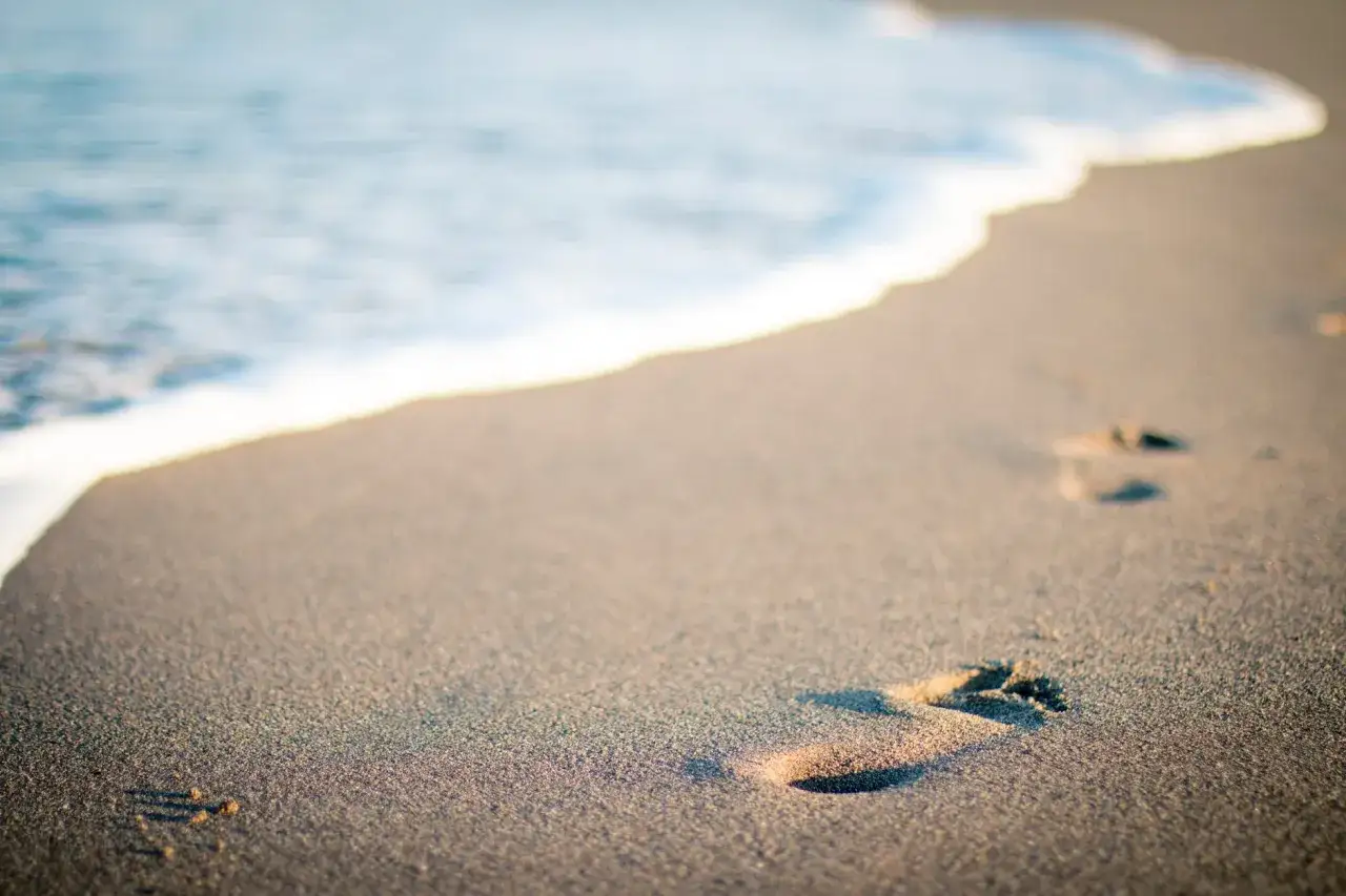 Ślady stóp na piaszczystej plaży, gdzie fale obmywają brzeg. Choć w Polsce jest tylko jedno morze, Bałtyk, to jego piękno jest niezmierzalne.