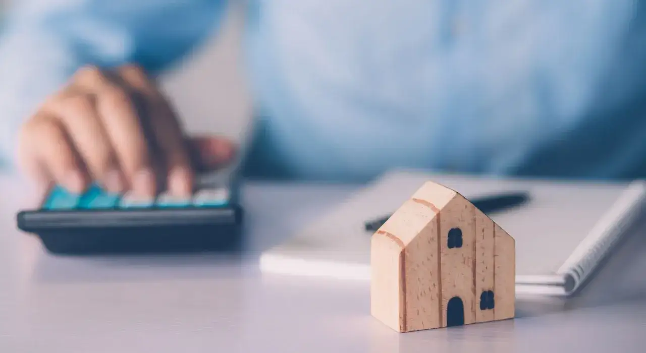 Drewniany domek, kalkulator i notatnik na biurku.